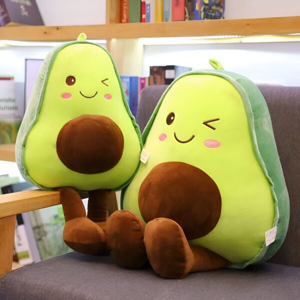 peluche-avocat-mignon-pour-fille-2a-2 Deux peluches en forme d'avocats souriants avec des joues roses et des yeux brodés. Elles sont assises sur un fauteuil en bois.