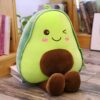 peluche-avocat-mignon-pour-fille-3a-1 Une peluche avocat souriante avec un noyau brun et des joues roses, assise sur un plancher en bois.