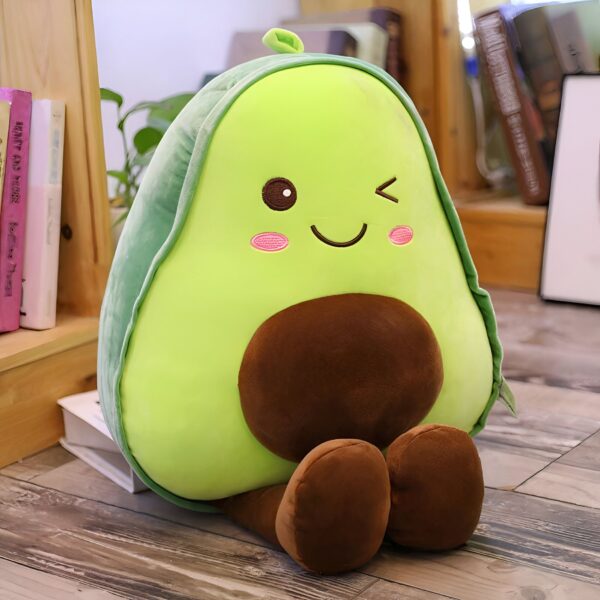 peluche-avocat-mignon-pour-fille-3a-1 Une peluche avocat souriante avec un noyau brun et des joues roses, assise sur un plancher en bois.
