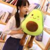 peluche-avocat-mignon-pour-fille-4a-2 Une jeune femme tenant un gros coussin en forme d'avocat avec un visage souriant.