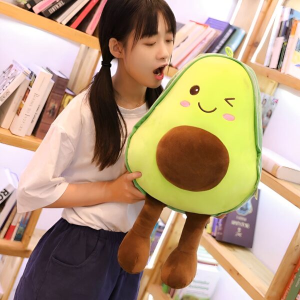 peluche-avocat-mignon-pour-fille-4a-2 Une jeune femme tenant un gros coussin en forme d'avocat avec un visage souriant.