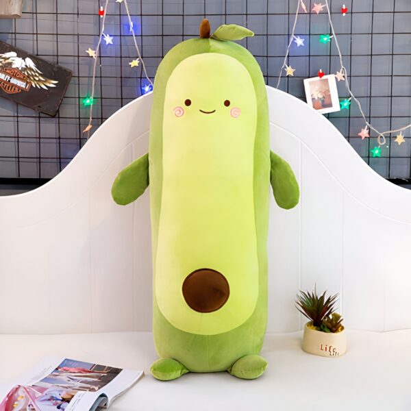 Coussin en forme d'avocat souriant avec des bras et des jambes, sur un lit blanc.