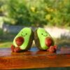 peluche-avocat-porte-cles-cadeau-fille-sac-a-dos-2a-1 Deux peluches en forme d'avocat souriants sont assis sur un banc en bois.