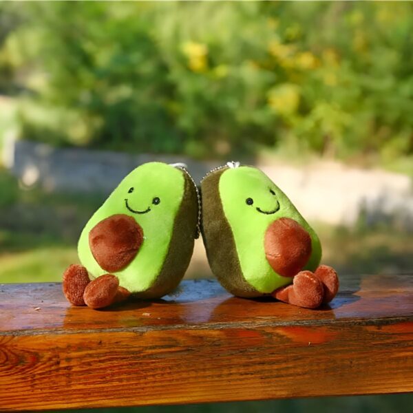 peluche-avocat-porte-cles-cadeau-fille-sac-a-dos-2a-1 Deux peluches en forme d'avocat souriants sont assis sur un banc en bois.