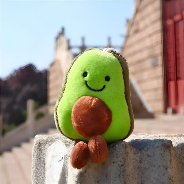 peluche-avocat-porte-cles-cadeau-fille-sac-a-dos-4a-2 Peluche avocat souriant assis sur un rocher avec un fond flou.
