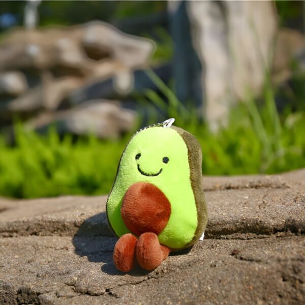 peluche-avocat-porte-cles-cadeau-fille-sac-a-dos-5a-2 Un adorable peluche en forme d'avocat avec un sourire et des petites jambes, assis sur un rocher.