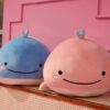 Deux baleines en peluche, une bleue et une rose, avec des visages souriants, posées sur un fond rose.