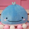 Une baleine en peluche bleue avec un sourire et des yeux noirs, entourée de petites boules roses et blanches.