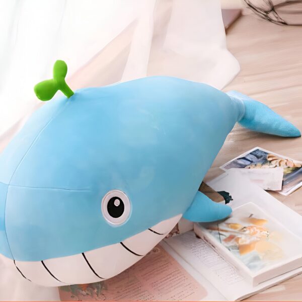 Une peluche bleue en forme de baleine avec un petit sourire et une feuille verte sur la tête.