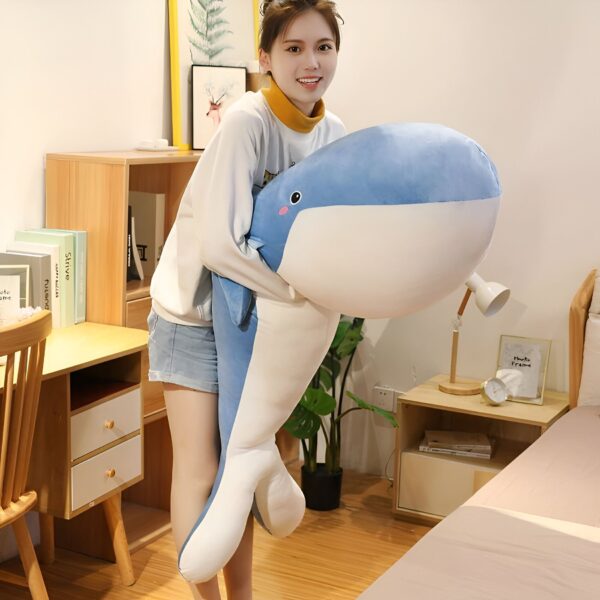 Une jeune femme souriante tenant une grande peluche bleue en forme de baleine.