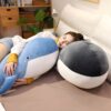Une femme dort sur un lit avec deux gros oreillers en forme de baleine, l'un bleu et l'autre gris.