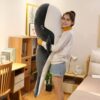 Une jeune femme souriante en short bleu tenant une grande peluche baleine noire et blanche.