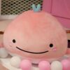 Une baleine rose en peluche avec un sourire et un petit nœud bleu sur la tête, entourée de boules roses et blanches.