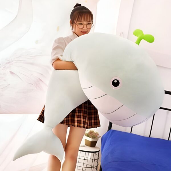 Une jeune femme souriante tenant une grande peluche baleine verte et blanche.