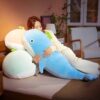 peluche-baleine-geante-pastel-xxl-cadeau-enfant-adulte-5a-1 Une femme se blottit contre un grand coussin en forme de baleine bleue, tenant un autre coussin en forme de baleine plus petit.