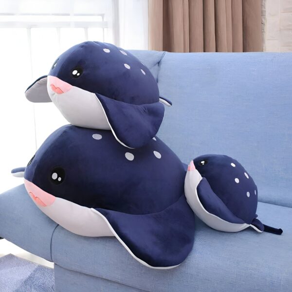 Trois peluches en forme de raie manta bleue avec des points blancs sur un canapé bleu.