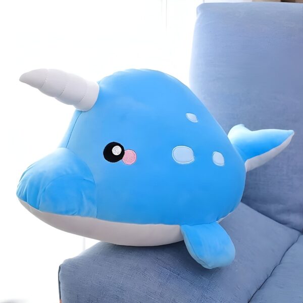 Une peluche en forme de narval bleu avec une corne blanche et des yeux noirs et roses.