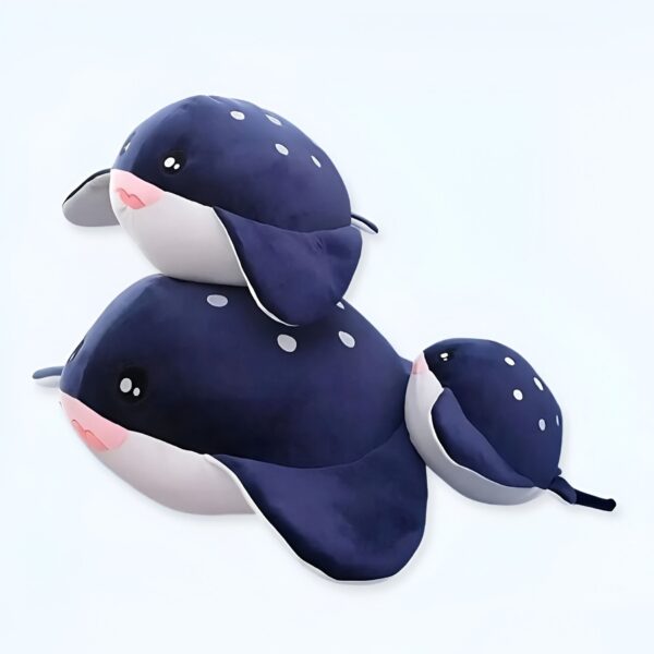 Trois peluches en forme de raie manta bleue à pois blancs, la plus grande est couchée, les deux plus petites sont sur elle.