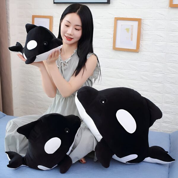 Une jeune femme souriante tenant trois peluches en forme d'orques noires et blanches.