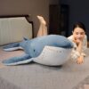 Une jeune femme souriante allongée sur un lit avec une grande peluche baleine bleue.