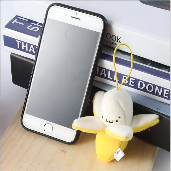 Un porte-clés en forme de banane jaune et blanche avec un visage souriant, sur une pile de livres à côté d'un smartphone.