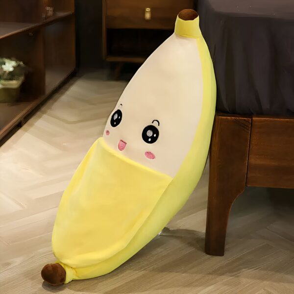 Un coussin en forme de banane jaune avec un visage souriant, posé à côté d'un lit en bois.