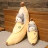 Deux peluches en forme de banane avec un chat gris à l'intérieur, l'une plus grande que l'autre. Les peluches sont posées sur un lit.