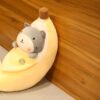 Un chat gris mignon enroulé dans une banane en peluche jaune.