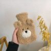 Une bouillotte en forme d'ours en peluche beige avec un visage brodé.