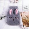 Une bouillotte en forme de lapin gris avec des oreilles roses. La bouillotte est en fourrure et a un visage souriant.