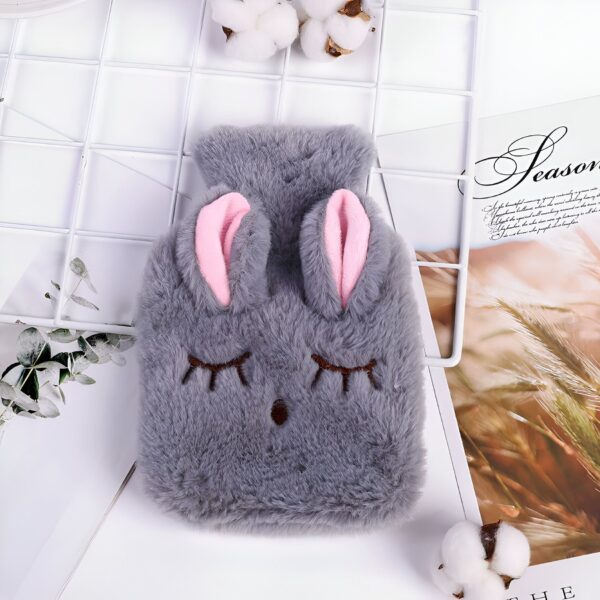 Une bouillotte en forme de lapin gris avec des oreilles roses. La bouillotte est en fourrure et a un visage souriant.