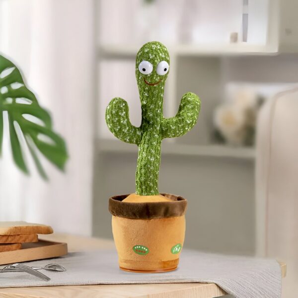 peluche-cactus-chantant-et-dansant-jouet-interactif-10a Un cactus en peluche souriant dans un pot en céramique marron. Le cactus a de grands yeux blancs et un sourire. Il est assis sur une table en bois. Il y a des couverts et une assiette en bois sur la table.