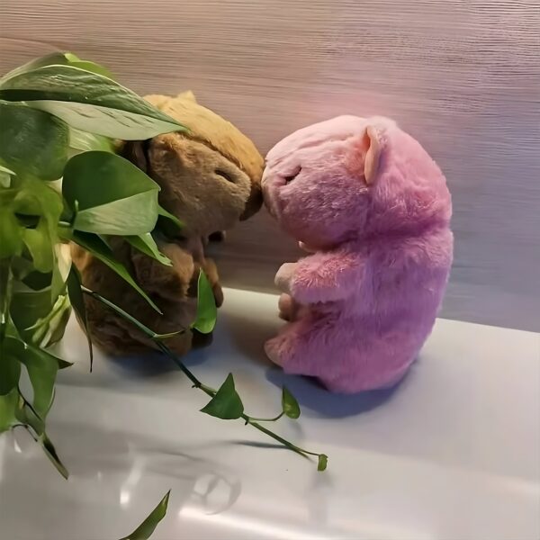 Deux peluches, l'une brune et l'autre rose, se font face sur un fond blanc. Une plante verte est visible à gauche de l'image.