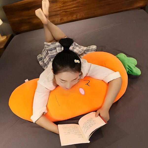 Une jeune femme est allongée sur un coussin en forme de carotte orange et lit un livre.