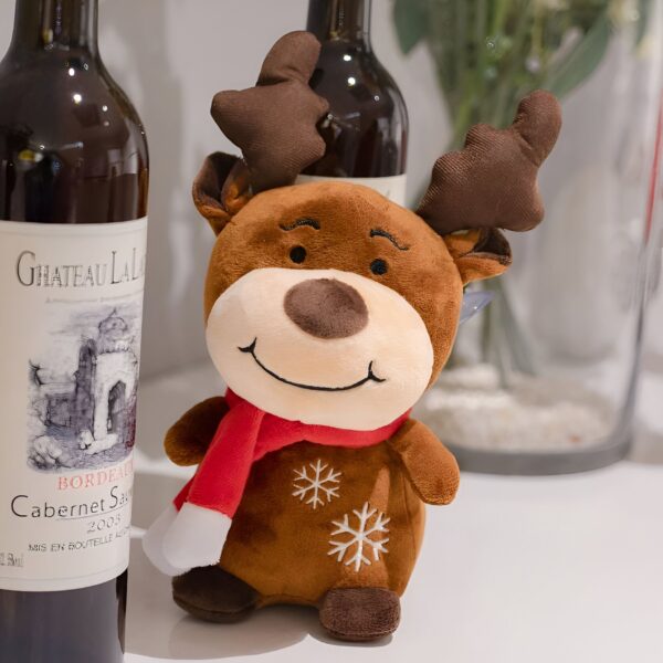 peluche-cerf-noel-jouet-doux-pour-enfants-2a-2 Un renne en peluche brun avec un foulard rouge et des flocons de neige sur son ventre, devant deux bouteilles de vin.