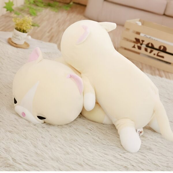 Deux peluches en forme de chat, l'une plus petite que l'autre, sont posées sur un tapis blanc. La plus grande est allongée et la plus petite est couchée sur elle.