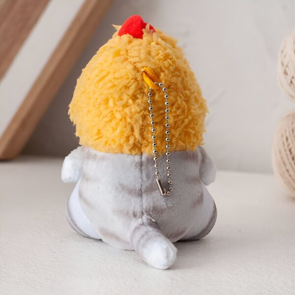 Porte-clés en peluche représentant un chat blanc et gris avec une crinière jaune et une crête rouge.