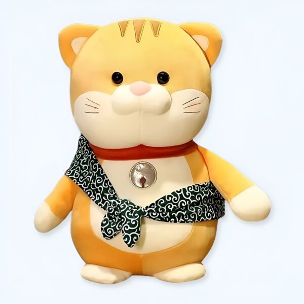 Une peluche de chat jaune portant un foulard vert avec des motifs. La peluche a un médaillon argenté autour du cou.
