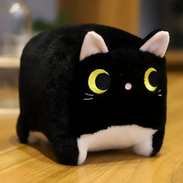 Une peluche de chat noir en forme de cube avec de grands yeux jaunes et un petit nez rose.