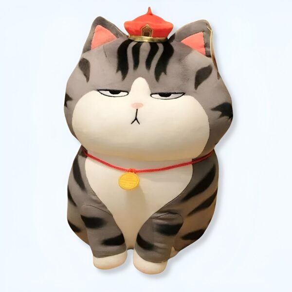 Peluche de chat gris et blanc portant un chapeau rouge et un collier rouge avec un médaillon jaune.