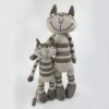 Deux peluches en forme de chat rayées de gris et de beige, debout l'une à côté de l'autre. Le plus grand chat a un sourire plus large.