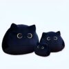 Trois peluches en forme de chat noir avec de grands yeux ronds. La plus grande peluche est au premier plan, les deux autres sont derrière.