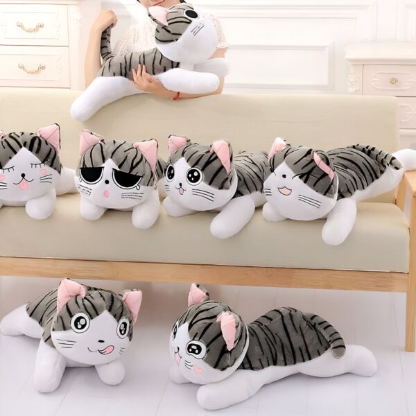 Six peluches de chat gris et blanc couchées sur un canapé.