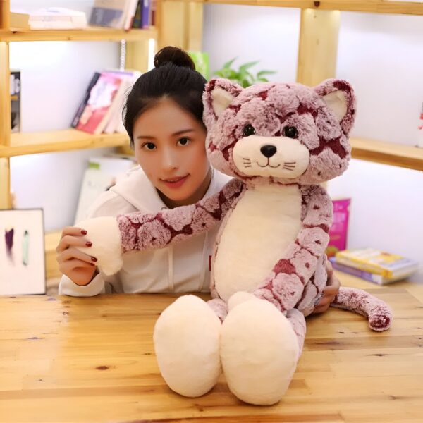 Une jeune femme souriante tient un grand chat en peluche rose et blanc. Le chat a de grands yeux noirs et un nez rose.