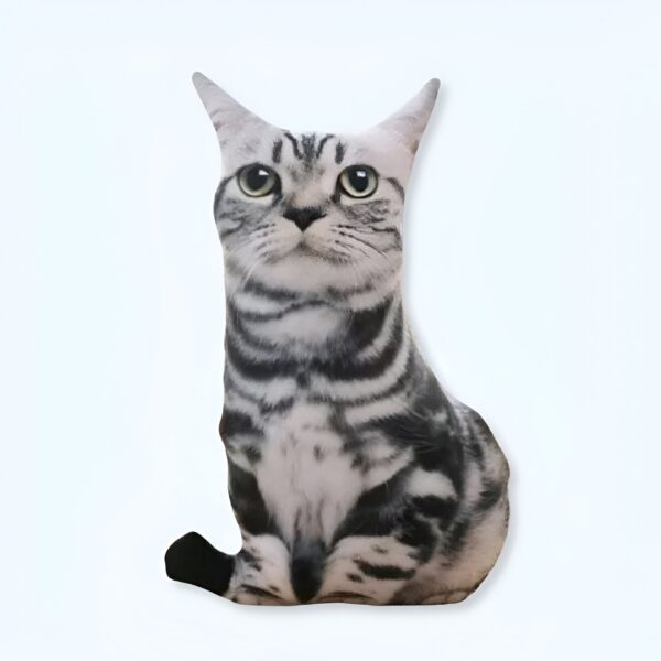 Un coussin en forme de chat gris et blanc assis sur un fond blanc.