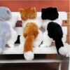 Trois peluches de chat assis sur un banc blanc. Le chat à gauche est gris et blanc, le chat au milieu est orange et blanc, et le chat à droite est noir et blanc.