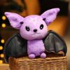Une peluche de chauve-souris violette avec des ailes noires et une étoile à cinq branches sur la tête.