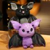 Deux chauves-souris en peluche, l'une noire avec une lune et l'autre violette avec une étoile, sont assises dans un panier en osier.