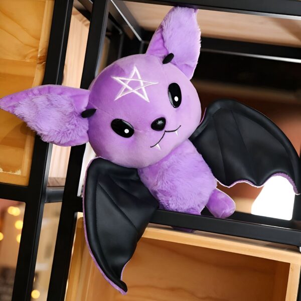 Une peluche de chauve-souris violette avec des ailes noires et une étoile à cinq branches sur le front.