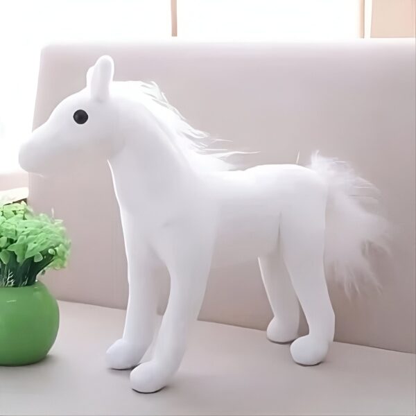 Une peluche blanche en forme de cheval avec une crinière et une queue blanches. Le cheval a de grands yeux noirs et se trouve sur un canapé blanc.
